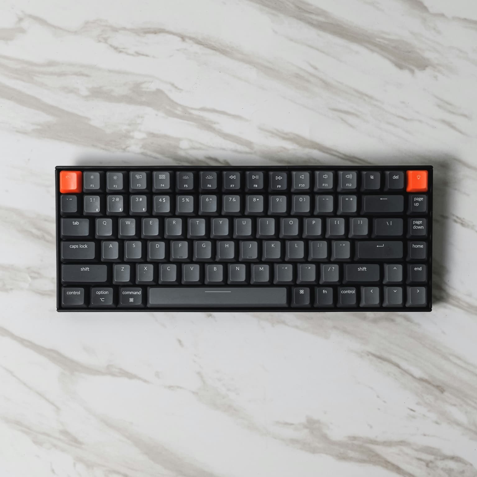 Compact mechanical keyboard with dark gray keycaps on a marble desk