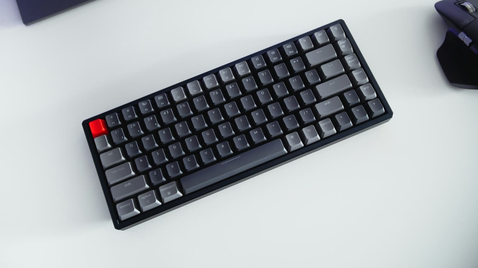 Compact mechanical keyboard with gray keycaps and a red Esc key on a white desk