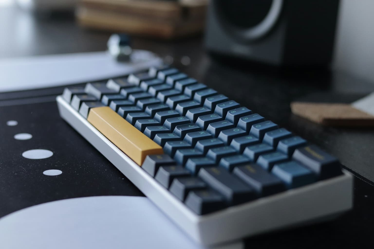 Compact mechanical keyboard with a yellow spacebar beside a desktop speaker