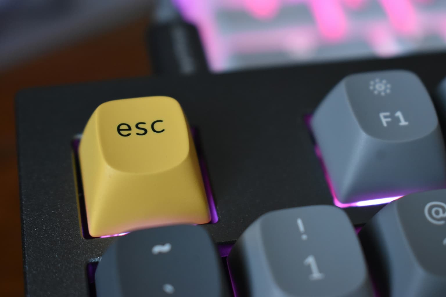 Close-up of a mechanical keyboard with a yellow Esc key and pink backlighting