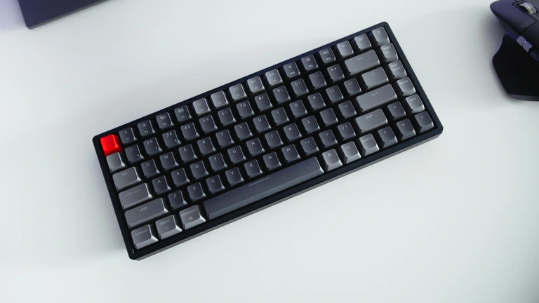 Compact mechanical keyboard with gray keycaps and a red Esc key on a white desk